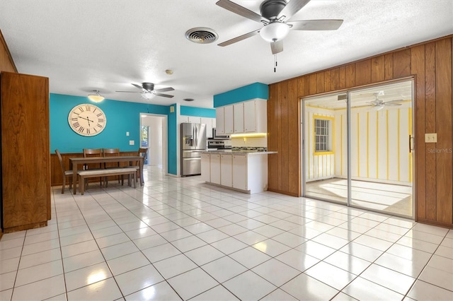living area with wooden walls, visible vents, ceiling fan, and a textured ceiling