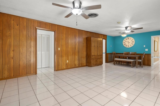 living area with wooden walls, visible vents, baseboards, and a ceiling fan