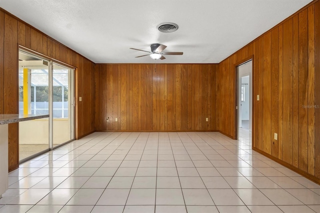 spare room with wood walls, baseboards, a ceiling fan, and visible vents