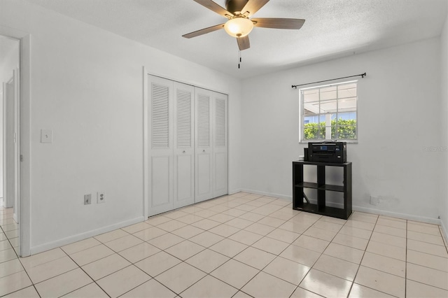 unfurnished bedroom with a closet, baseboards, light tile patterned floors, a textured ceiling, and ceiling fan