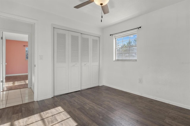 unfurnished bedroom with dark wood-type flooring, a closet, baseboards, and a ceiling fan