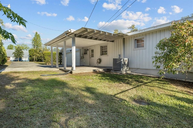 rear view of house with a carport, a patio, board and batten siding, central AC unit, and a yard
