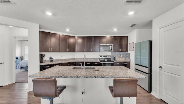 613 Sarner Pass Way, Winter Haven, FL 33881 - kitchen featuring appliances with stainless steel finishes, a kitchen breakfast bar, dark brown cabinetry, light wood finished floors, and a textured ceiling