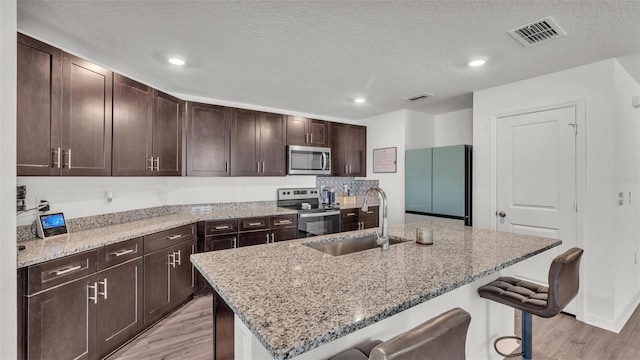 613 Sarner Pass Way, Winter Haven, FL 33881 - kitchen with appliances with stainless steel finishes, light wood finished floors, a breakfast bar, light stone counters, and a textured ceiling