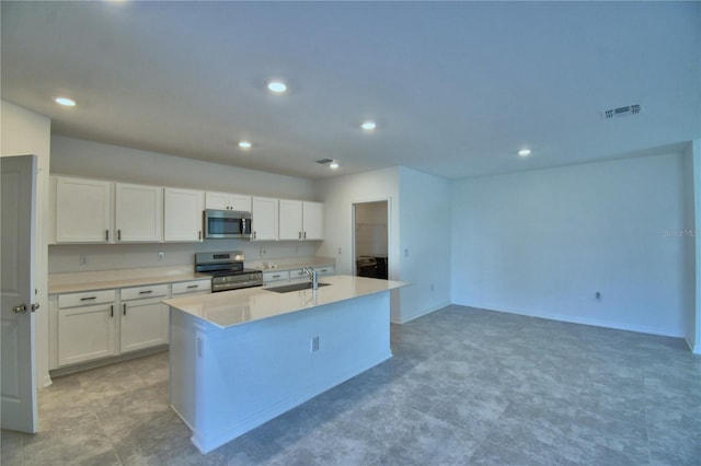 kitchen with white cabinets, stainless steel appliances, a sink, a center island with sink, and light countertops