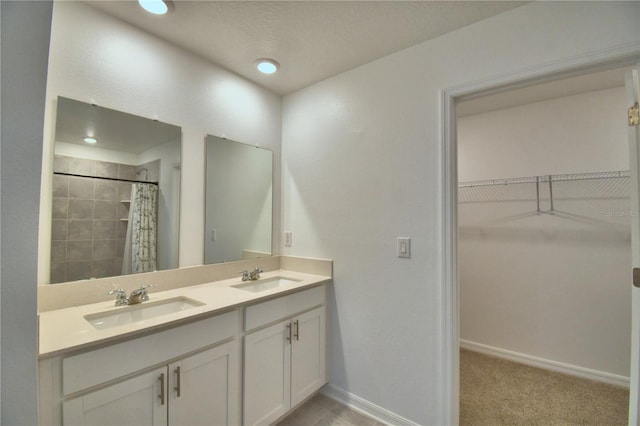 bathroom featuring a walk in closet, baseboards, a sink, and double vanity