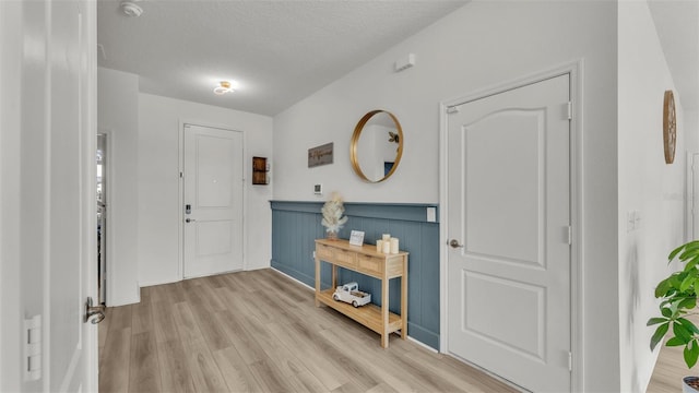 entrance foyer with wainscoting, light wood-style floors, and a textured ceiling