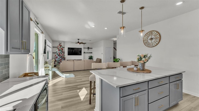 kitchen featuring a center island, hanging light fixtures, light wood-style flooring, gray cabinetry, and visible vents