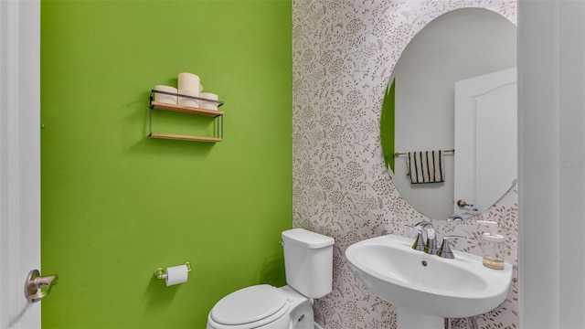 half bathroom with toilet, a sink, and wallpapered walls