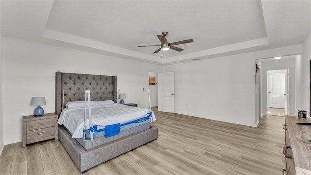 bedroom featuring a raised ceiling, light wood-type flooring, baseboards, and ceiling fan