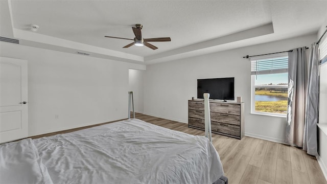 bedroom with baseboards, a tray ceiling, visible vents, and light wood-style flooring