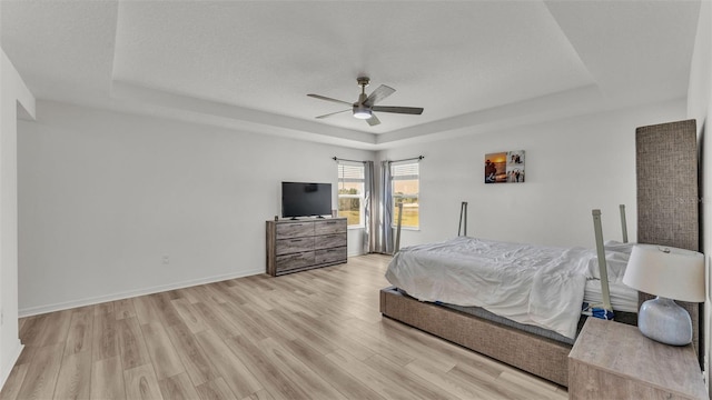 bedroom with baseboards, a tray ceiling, light wood-style floors, and ceiling fan