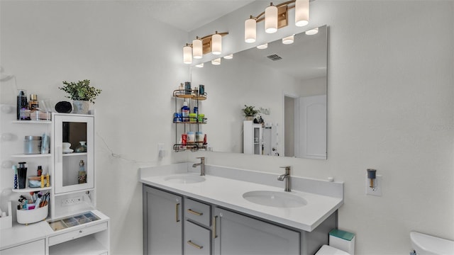bathroom featuring toilet, visible vents, a sink, and double vanity
