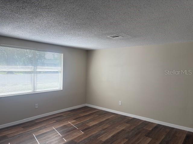 4830 Melody Ln, Lakeland, FL 33805 - spare room featuring a textured ceiling, baseboards, dark wood-style floors, and visible vents