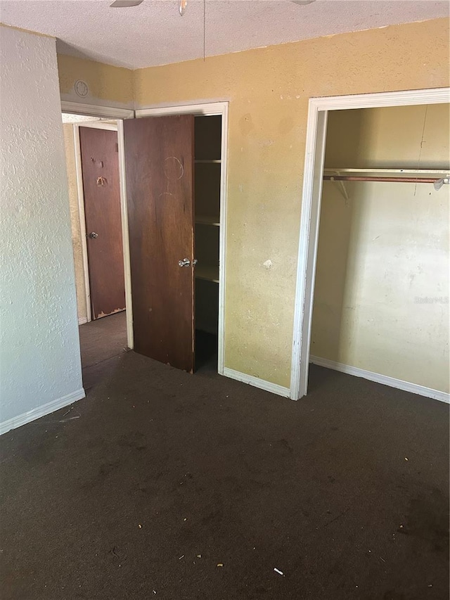 unfurnished bedroom with a textured wall, two closets, carpet floors, baseboards, and a textured ceiling