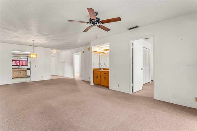 unfurnished living room featuring ceiling fan with notable chandelier, visible vents, carpet, and a sink