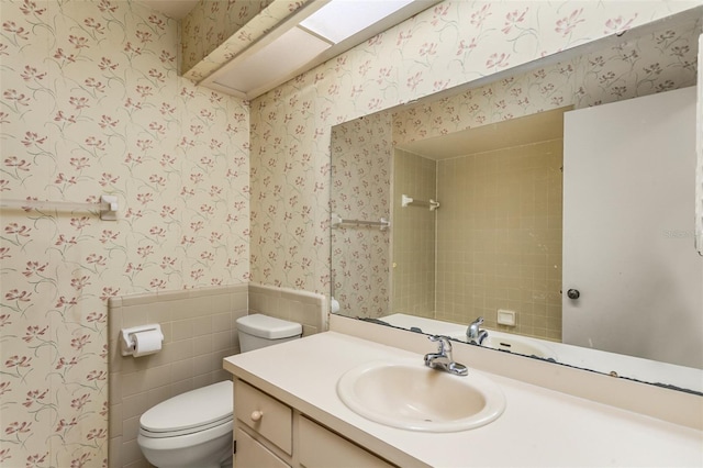 full bath with toilet, wainscoting, wallpapered walls, a shower, and vanity