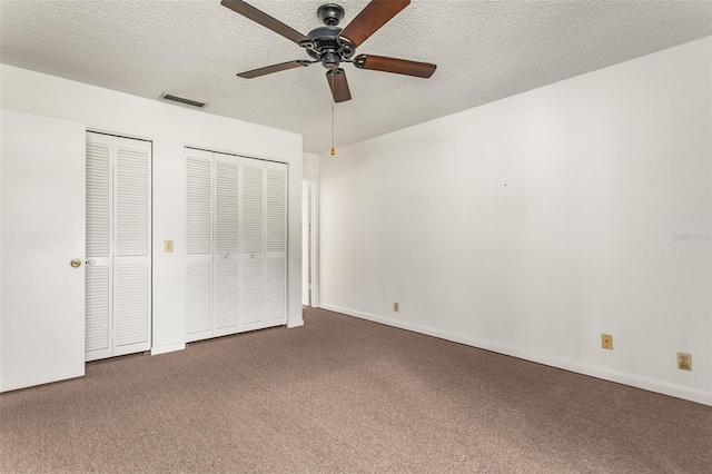 unfurnished bedroom featuring multiple closets, visible vents, a ceiling fan, a textured ceiling, and carpet flooring
