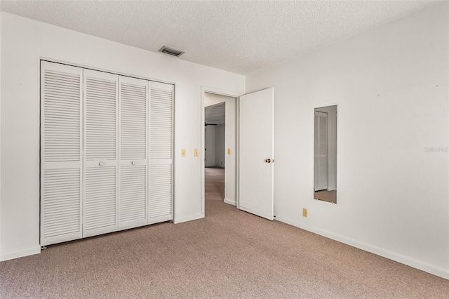 unfurnished bedroom featuring a textured ceiling, a closet, baseboards, carpet flooring, and visible vents
