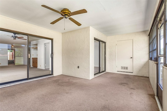 carpeted spare room featuring a textured wall, visible vents, and ceiling fan