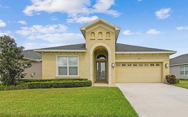 mediterranean / spanish-style home featuring concrete driveway, a front lawn, a garage, stucco siding, and roof with shingles