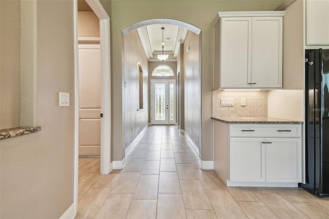 interior space with arched walkways, backsplash, ornamental molding, light stone countertops, and freestanding refrigerator