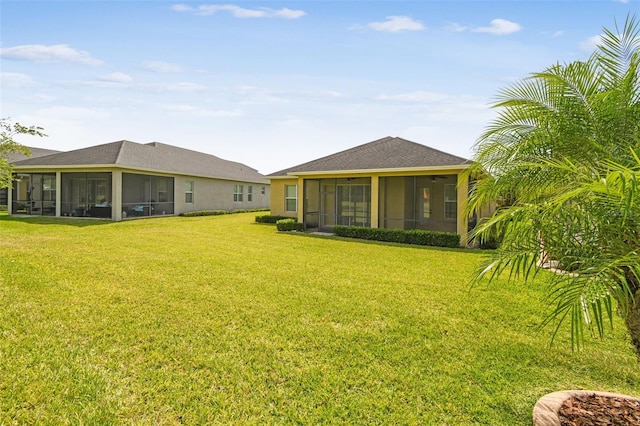 back of property with a lawn, a sunroom, and roof with shingles