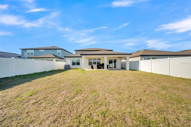 rear view of house with a lawn, a patio area, a fenced backyard, and central AC