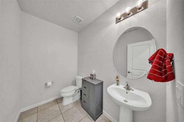 half bathroom featuring a sink, a textured ceiling, toilet, visible vents, and tile patterned flooring