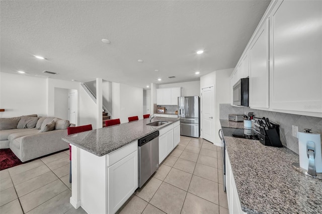 kitchen with stainless steel appliances, backsplash, a sink, open floor plan, and white cabinetry