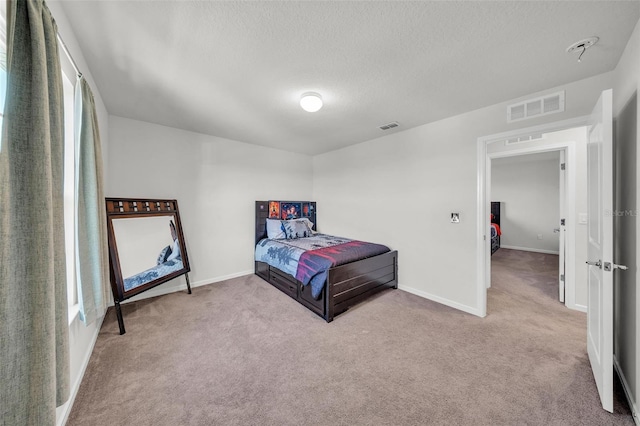 carpeted bedroom featuring a textured ceiling, visible vents, and baseboards