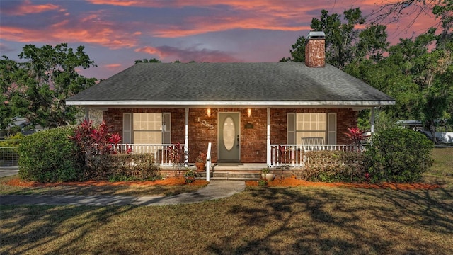 view of front facade with a chimney, a front lawn, roof with shingles, and covered porch
