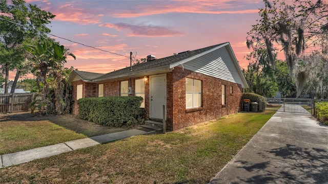 property exterior at dusk with fence, a lawn, entry steps, and brick siding