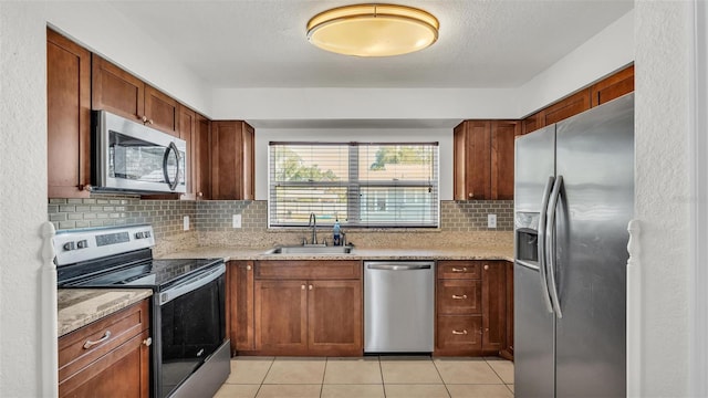 kitchen with a sink, decorative backsplash, appliances with stainless steel finishes, light stone counters, and light tile patterned floors