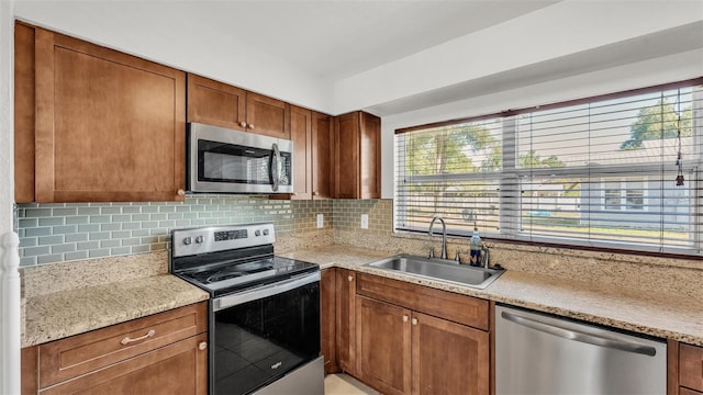 kitchen featuring a sink, decorative backsplash, brown cabinets, light stone countertops, and appliances with stainless steel finishes