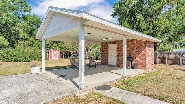 view of patio / terrace with fence, a carport, an outbuilding, and a storage shed