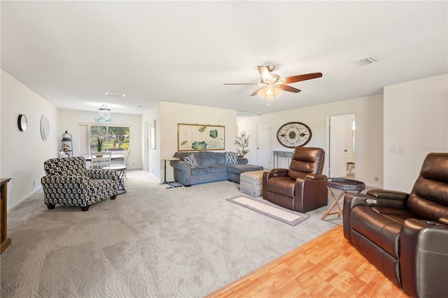 living room featuring a textured ceiling, visible vents, a ceiling fan, and light colored carpet