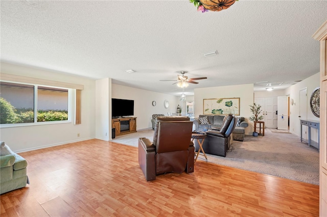 living room with baseboards, a ceiling fan, a textured ceiling, and light wood-style flooring