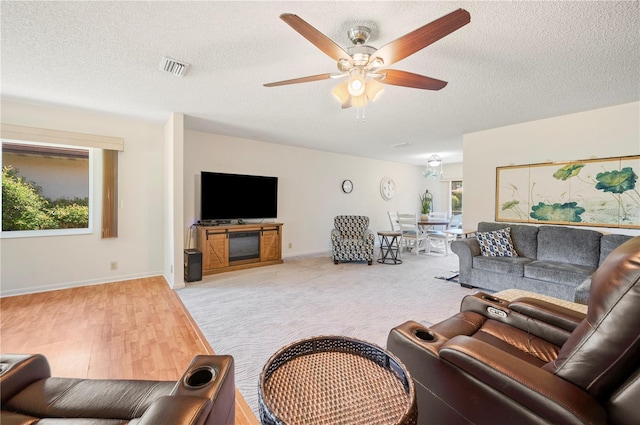 living room with baseboards, a ceiling fan, visible vents, and a textured ceiling