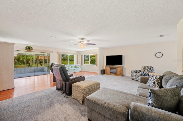 living room featuring ceiling fan, wood finished floors, a textured ceiling, and visible vents