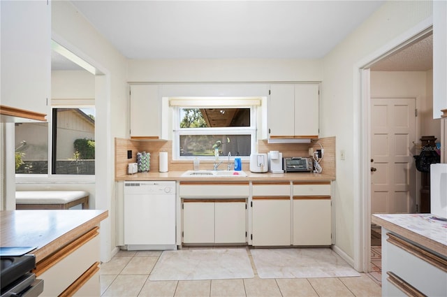 kitchen with light countertops, dishwasher, decorative backsplash, and a sink
