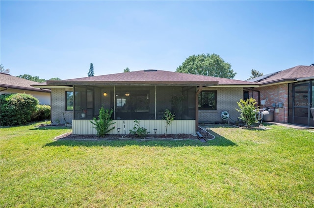 back of property with a sunroom, a lawn, and brick siding