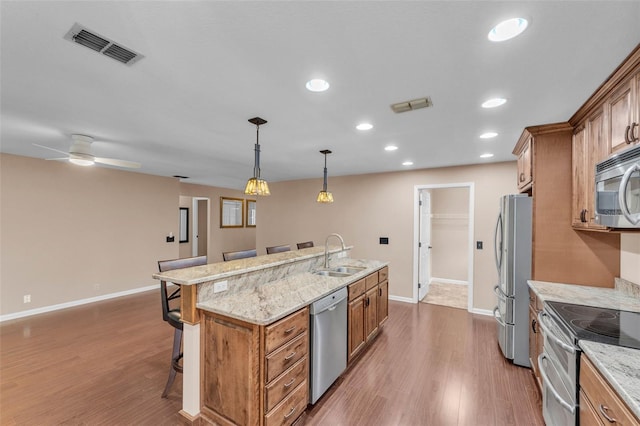 kitchen featuring brown cabinets, appliances with stainless steel finishes, a sink, a kitchen breakfast bar, and visible vents