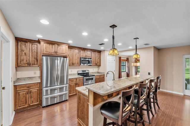 kitchen featuring visible vents, wood finished floors, a breakfast bar, brown cabinets, and appliances with stainless steel finishes