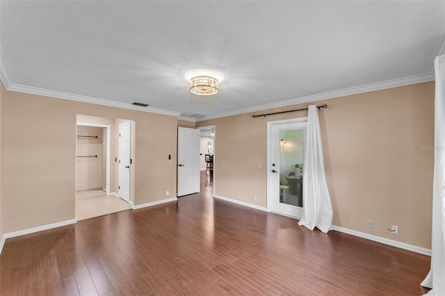 spare room with baseboards, ornamental molding, wood finished floors, and visible vents