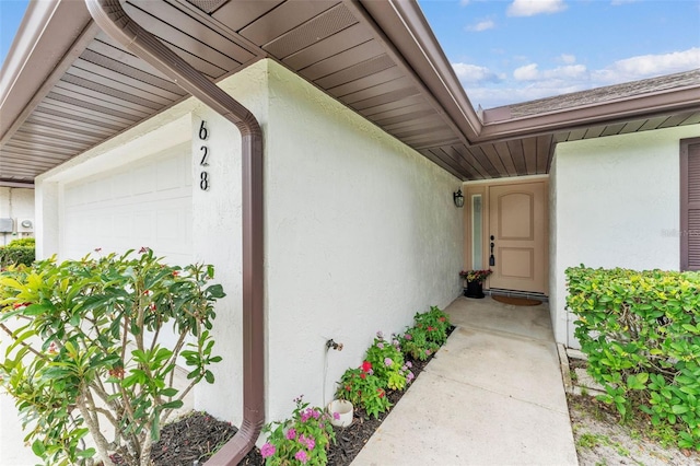 view of exterior entry with an attached garage and stucco siding