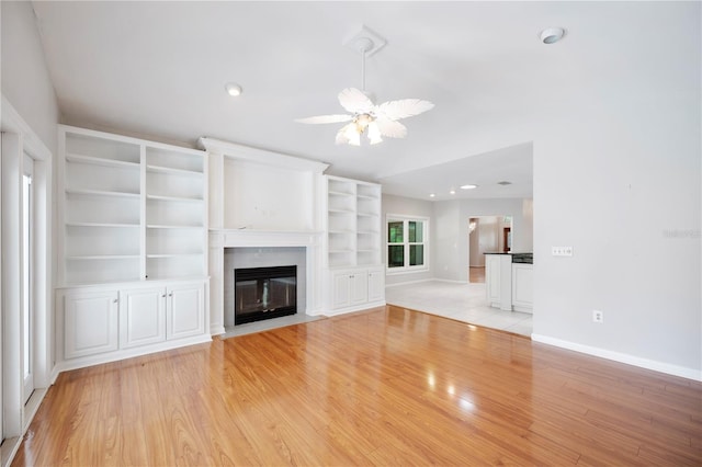 unfurnished living room featuring baseboards, light wood-type flooring, a fireplace with flush hearth, and ceiling fan