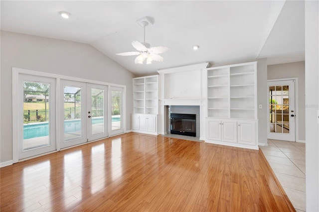 unfurnished living room with french doors, lofted ceiling, light wood finished floors, ceiling fan, and a fireplace with flush hearth