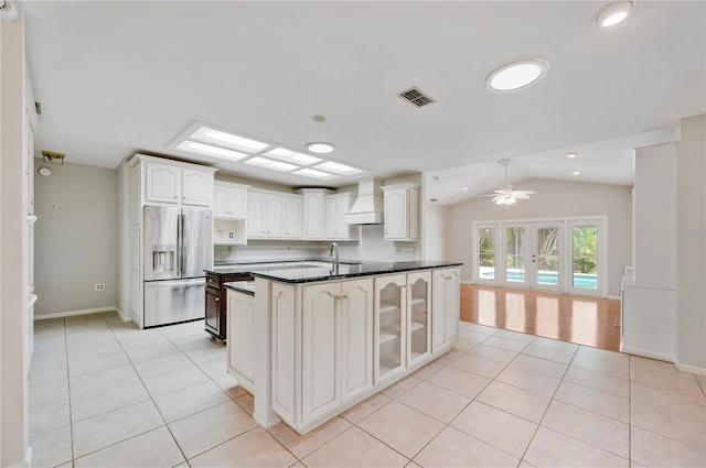 kitchen featuring stainless steel fridge, custom range hood, light tile patterned floors, glass insert cabinets, and vaulted ceiling