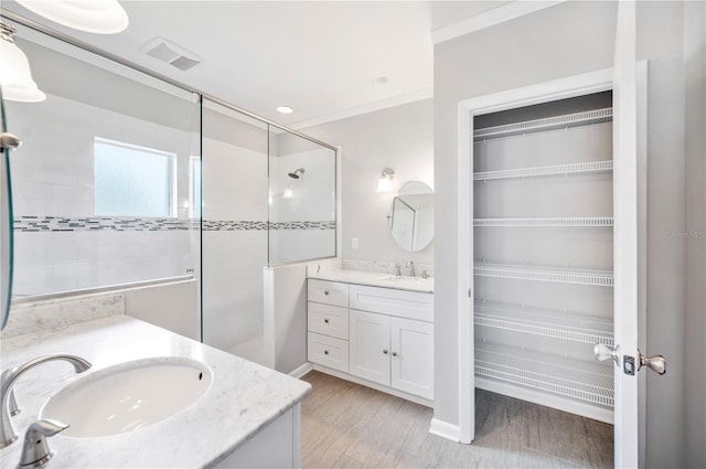 bathroom featuring a shower stall, vanity, a walk in closet, crown molding, and wood finished floors